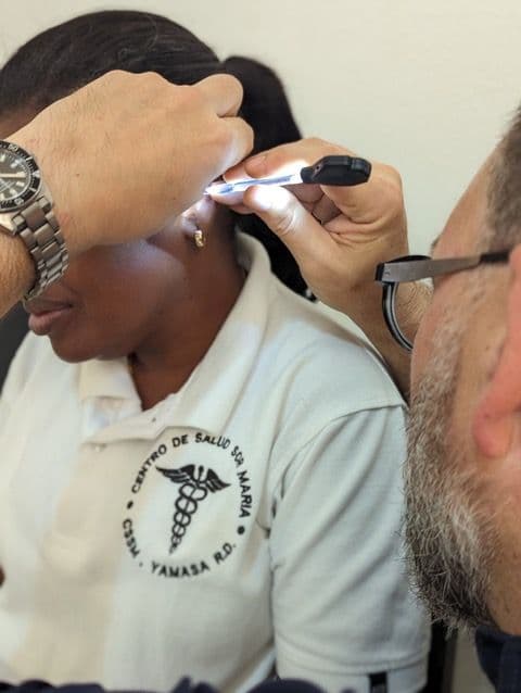 A Perry-Medico clinician using a lighted otoscope to examine the ear of a staff member from the Centro de Salud Sra Maria in Yamasa